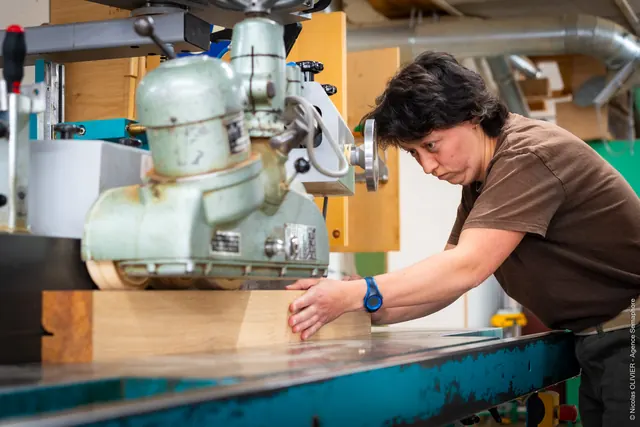 Menuiserie Baron : une artisane guide une pièce de bois sur la machine